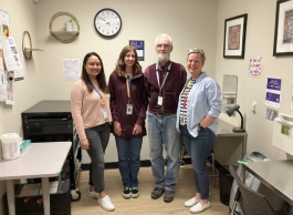 Four people wearing casual clothing and lanyards pose together in a medical office