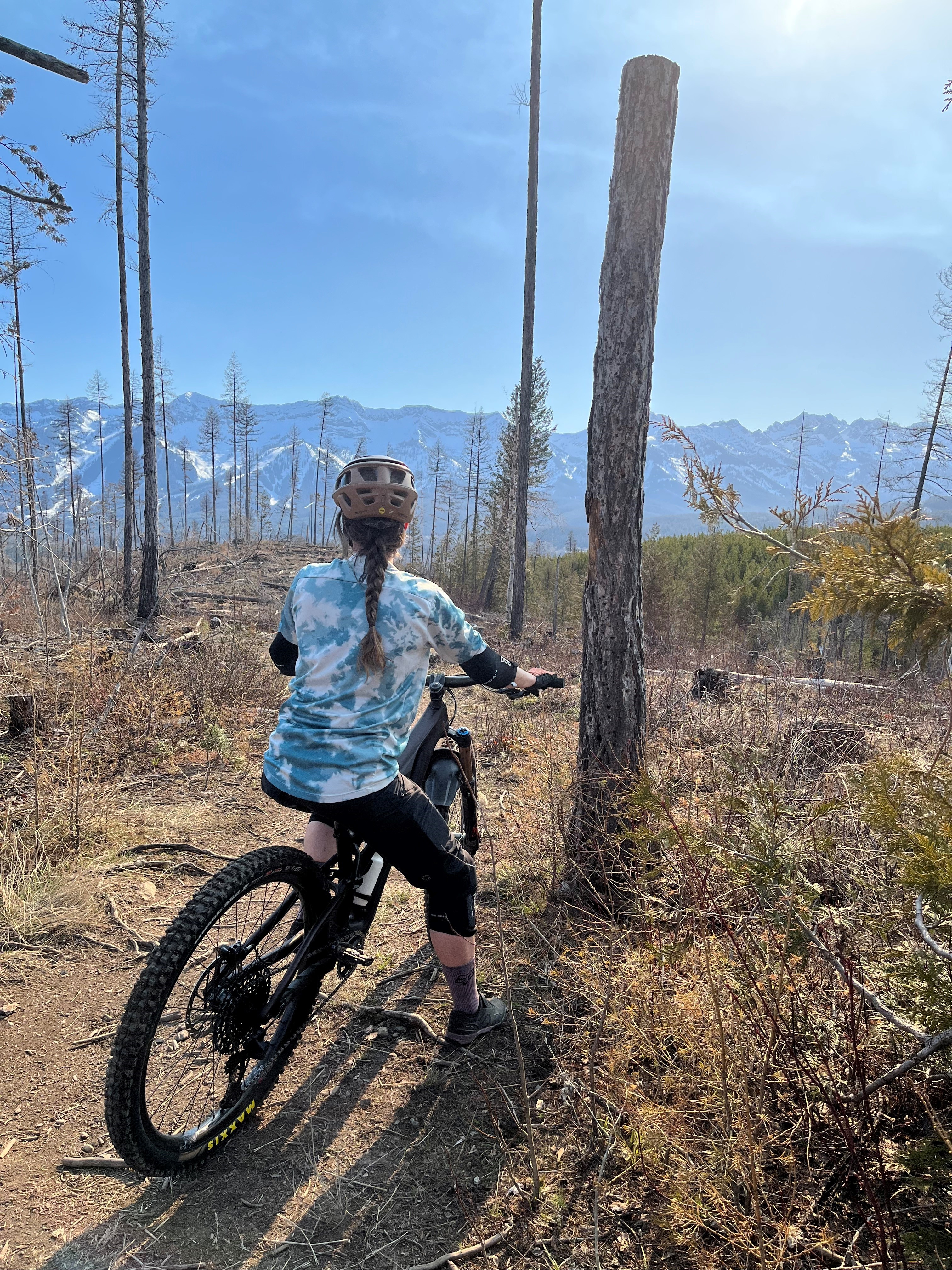 A woman with a braid in her hair wears a helmet while going for a mountain bike ride in the forest area with a Mountain View