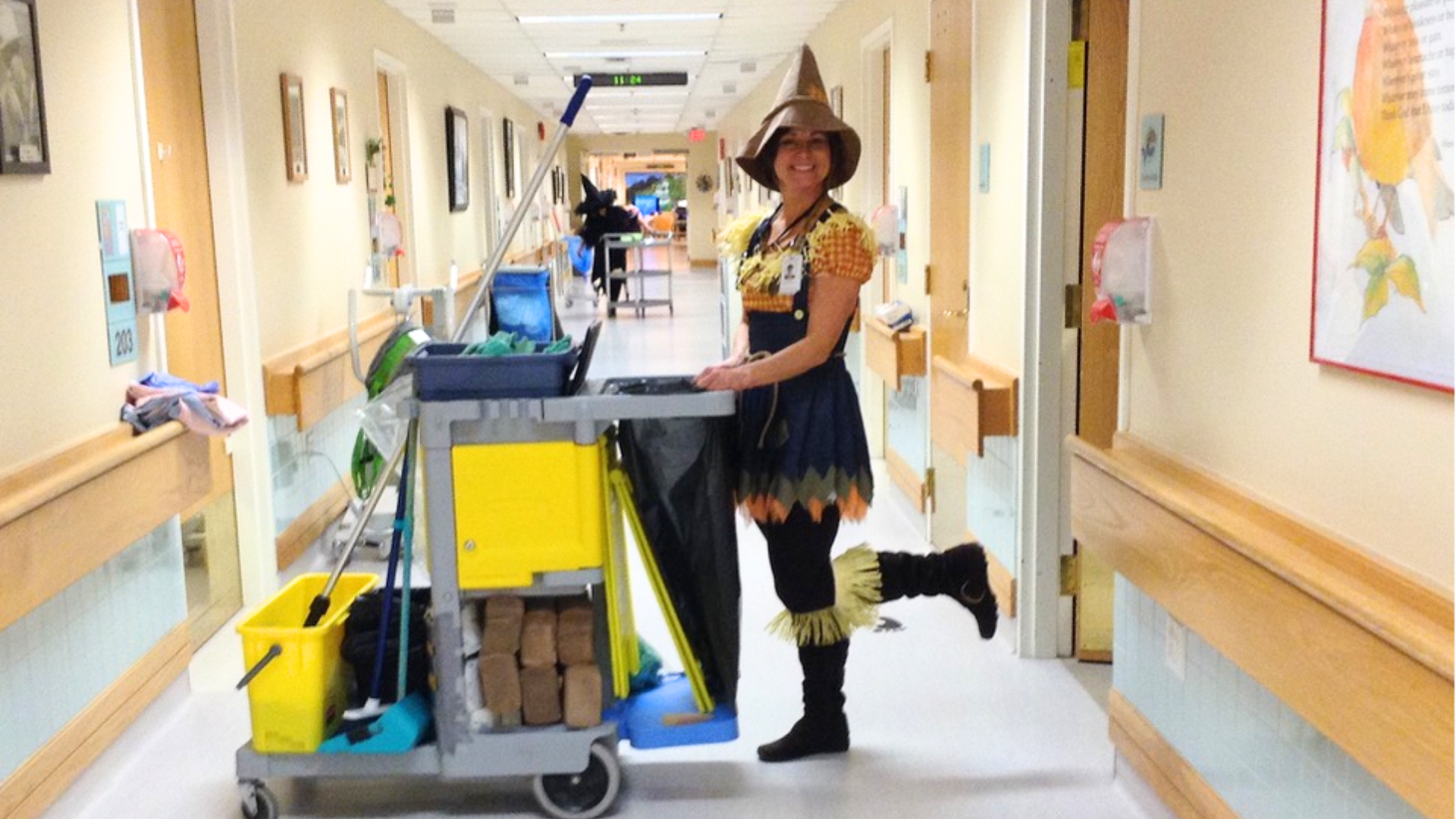 A woman pushing a cleaning cart in a hospital, dressed as a scarecrow for Halloween