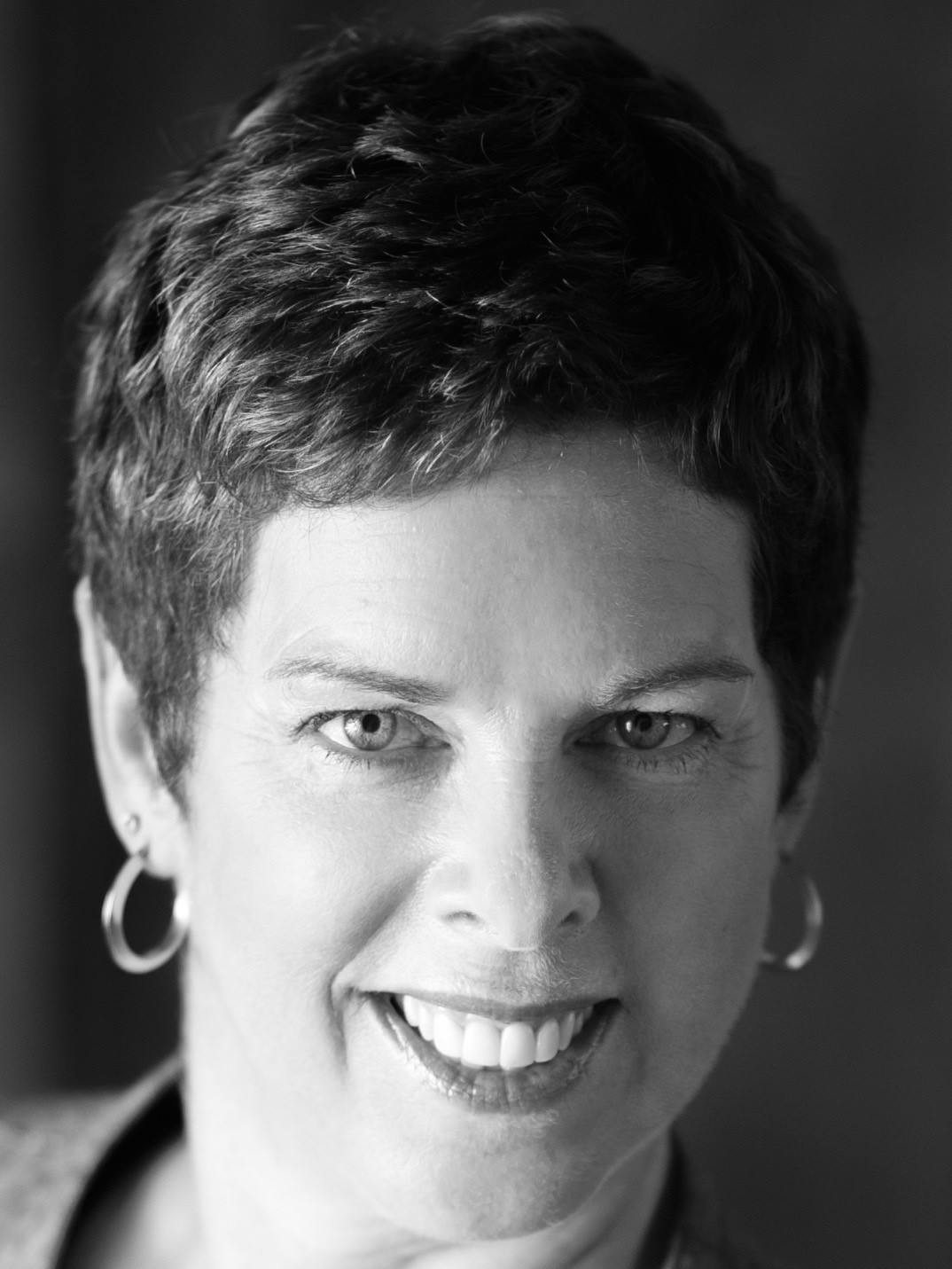A black and white photo of a woman with short hair, wearing hoop earrings.