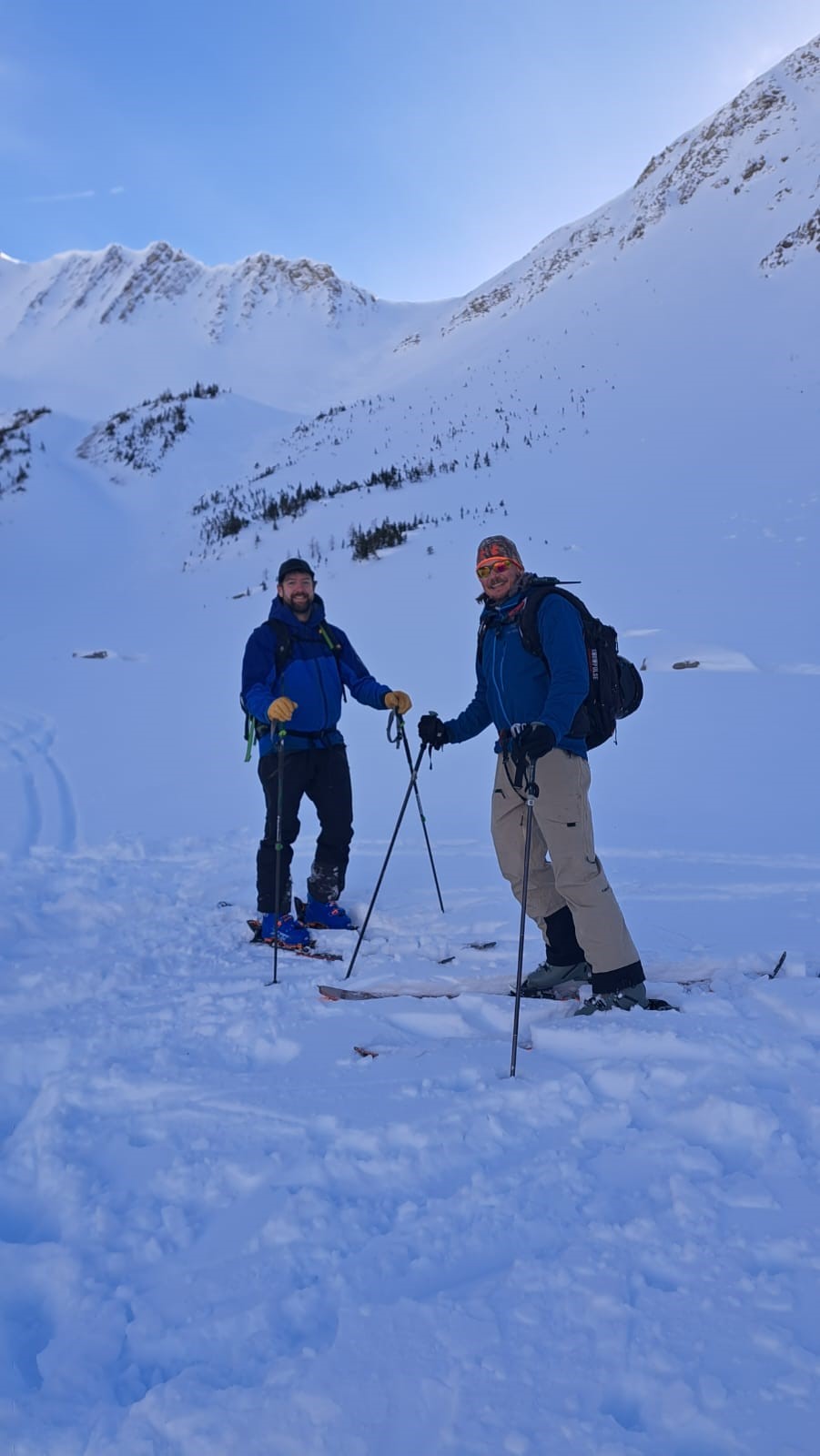 Two men on skis in snow with mountain behind them