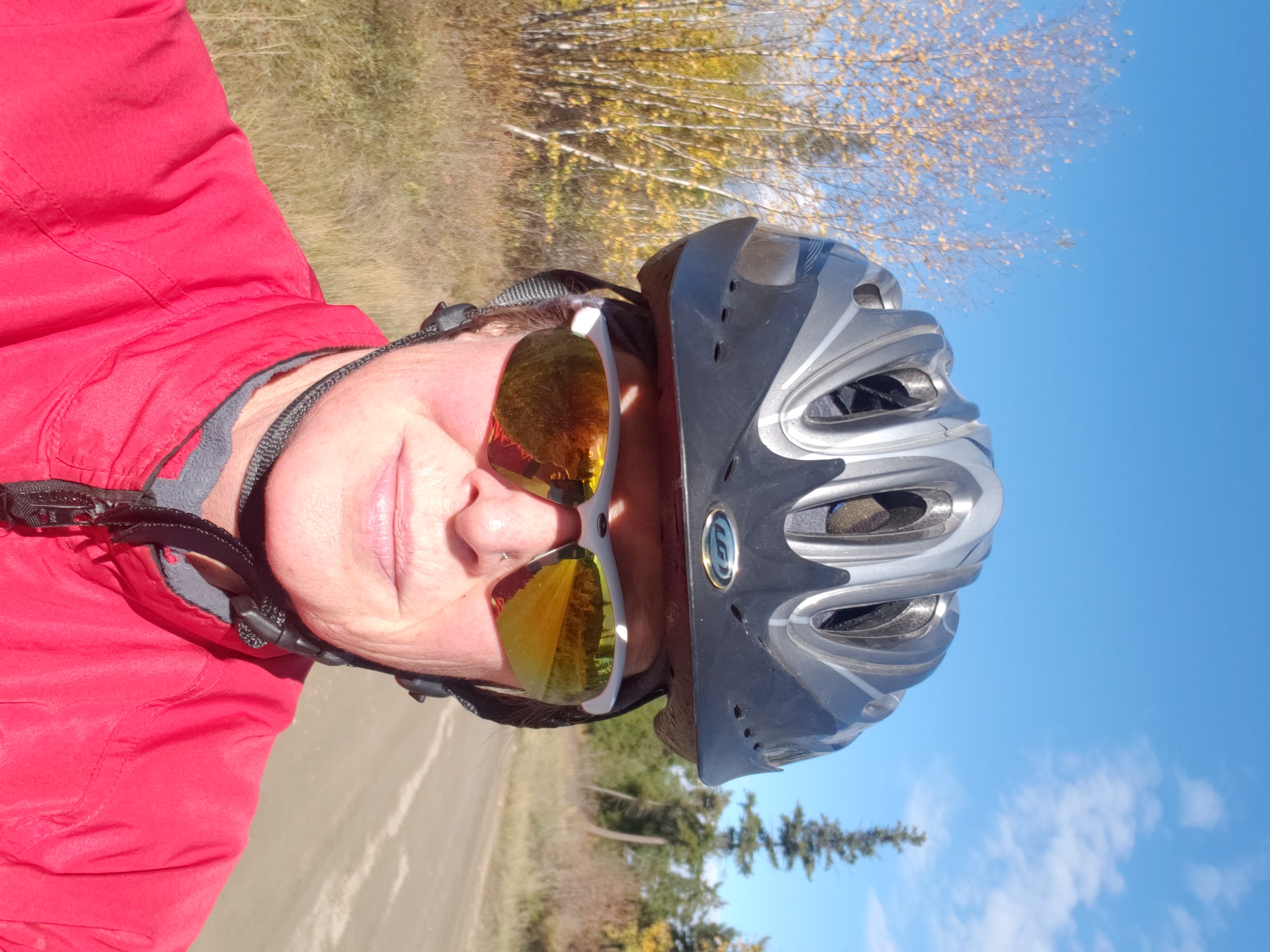 A selfie of a woman wearing a red jacket, sunglasses and a biking helmet.