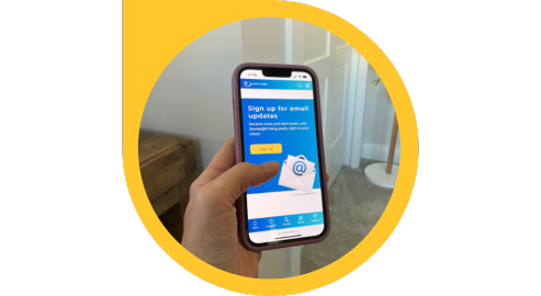 A hand holds a cell phone that shows a web page with text that says Sign up for email updates