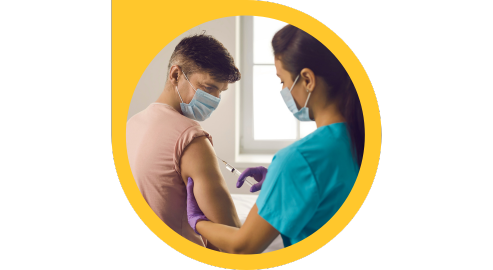 A health-care professional, wearing scrubs, gloves and a mask, gives an injection a patient who is also wearing a mask.