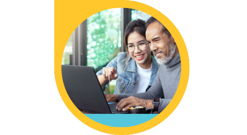 A young Asian girl in round glasses sits next to an older Asian man with a grey beard and turtleneck on front of a laptop
