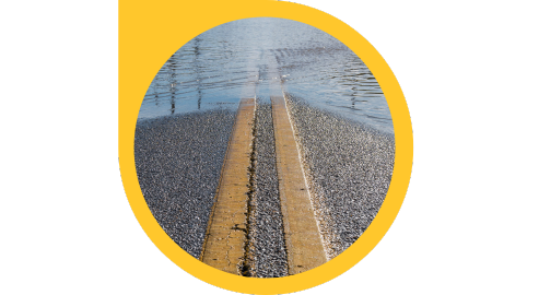 Water begins to cover a road with two large yellow lines running through the middle.