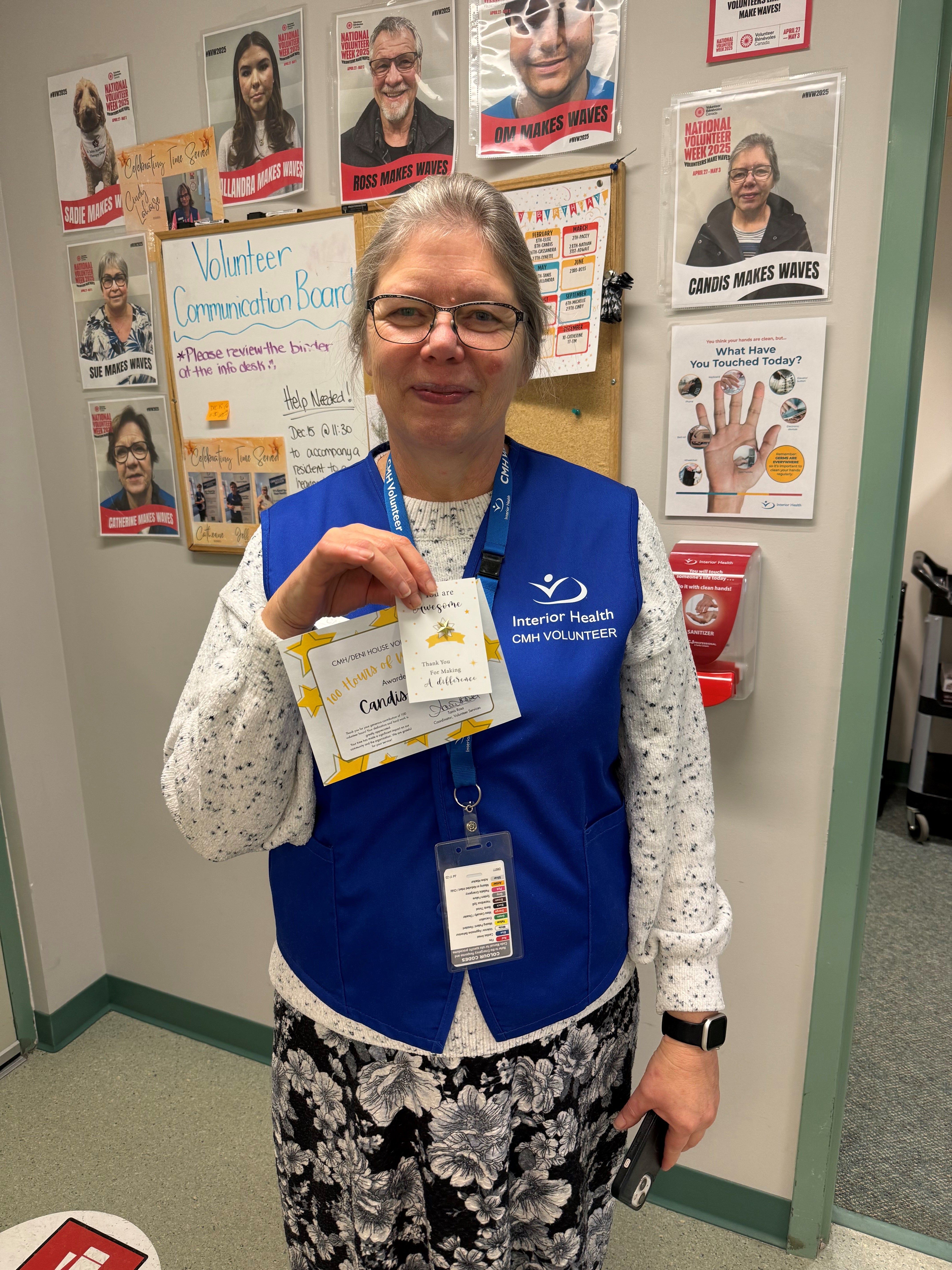 A person wearing a blue vest holds up a certificate in front of a wall of honour.