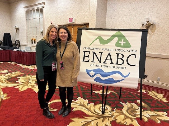 Two people in business attire wearing lanyards stand next to a sign with the initials ENABC in a hotel conference room.