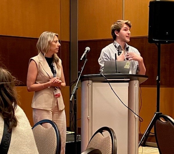 Two people stand at a podium present in a conference hall.
