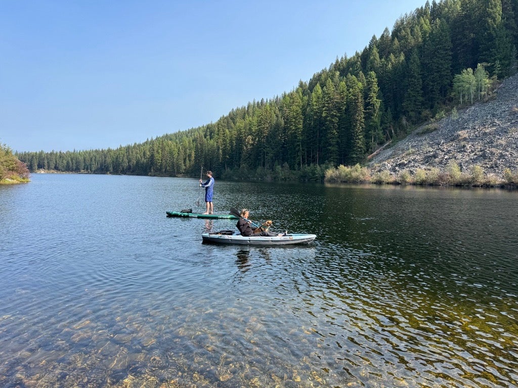 Two people float on a lake on a sunny day. One is on a stand-up paddleboard, the other on a canoe.