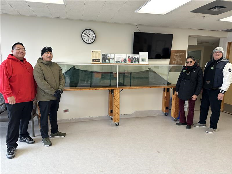 A group of four people in winter clothing stand in a lobby next to a glass-encased canoe.