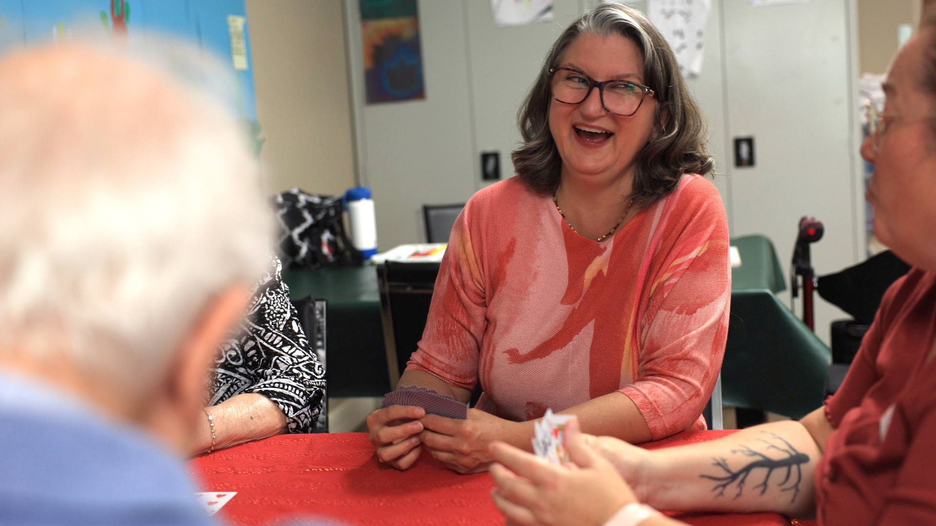 A woman in a red shirt is laughing while playing cards.