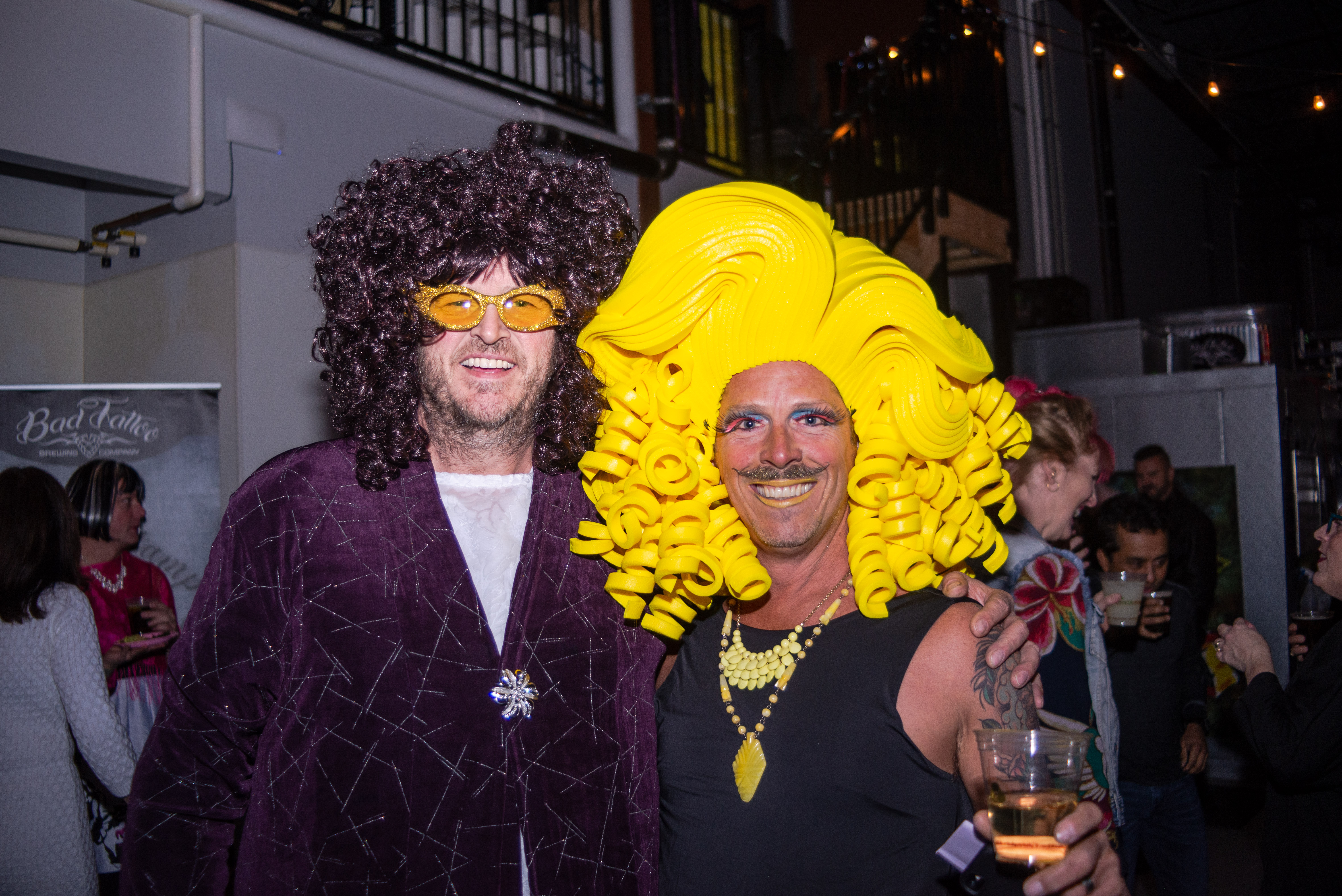 Two men wearing vibrant dress including large wigs at a drag performance