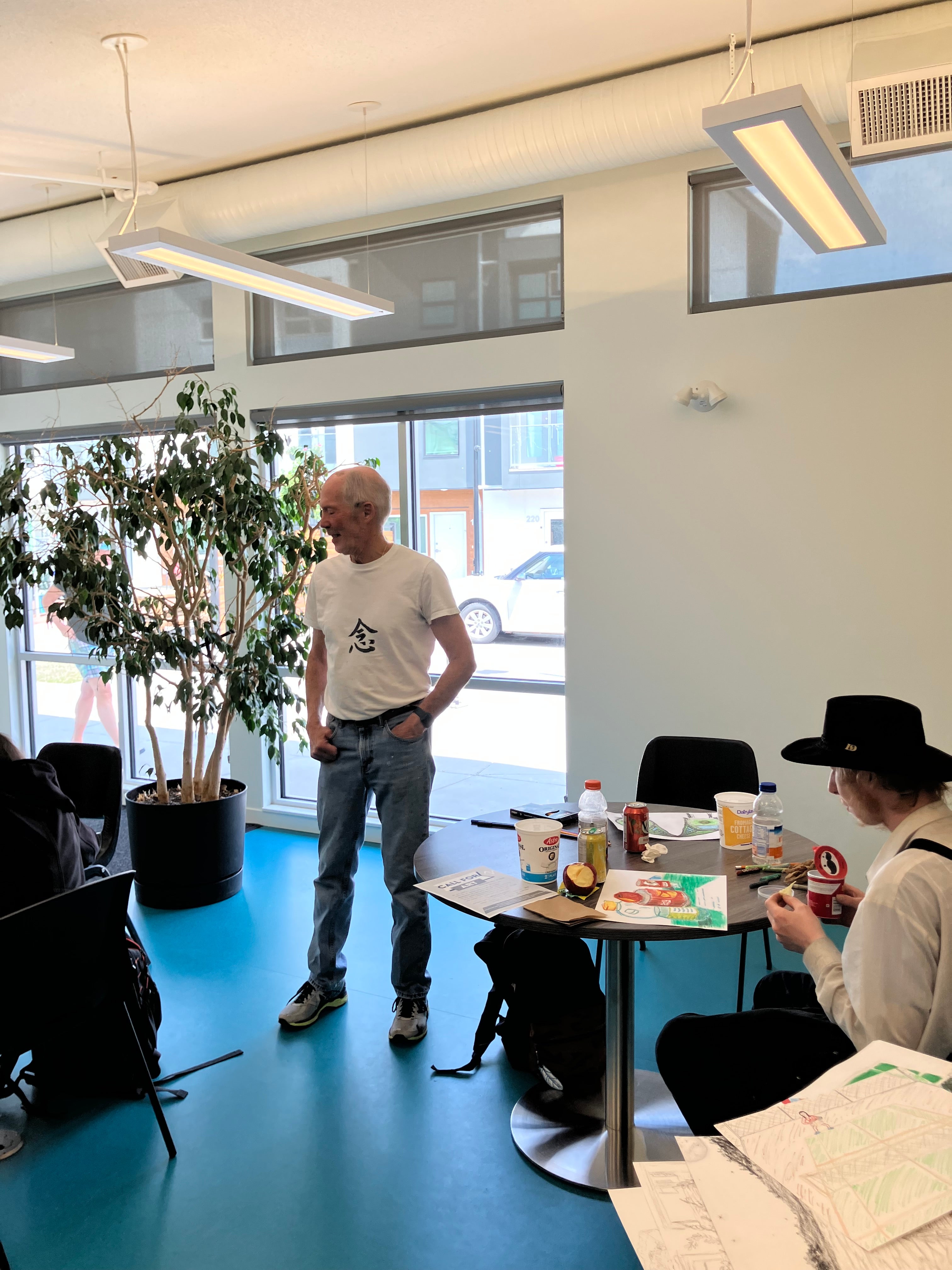A person in a white t-shirt stands at the front of room watching students draw.