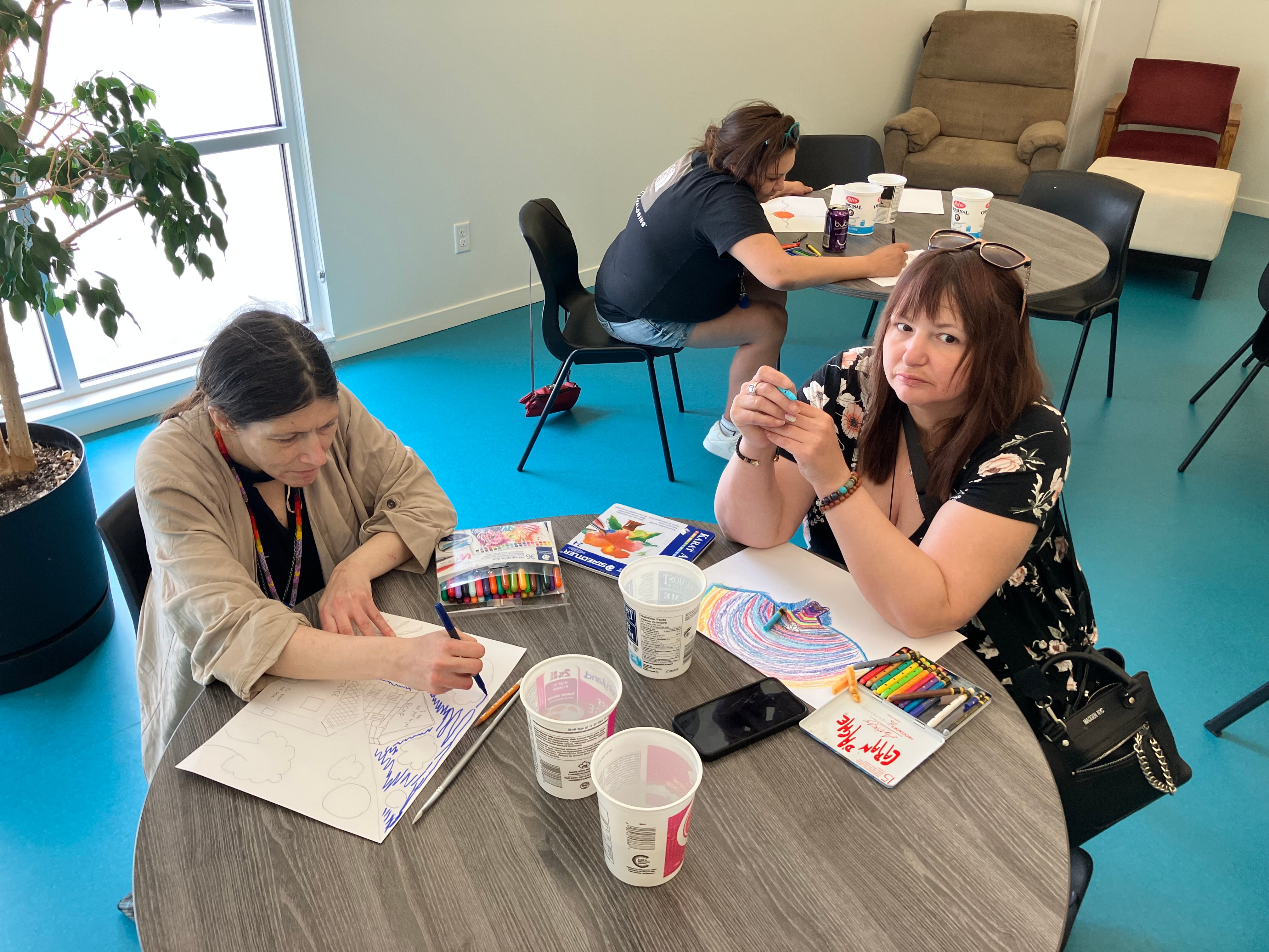 Three people sitting at two round tables colouring and drawing.