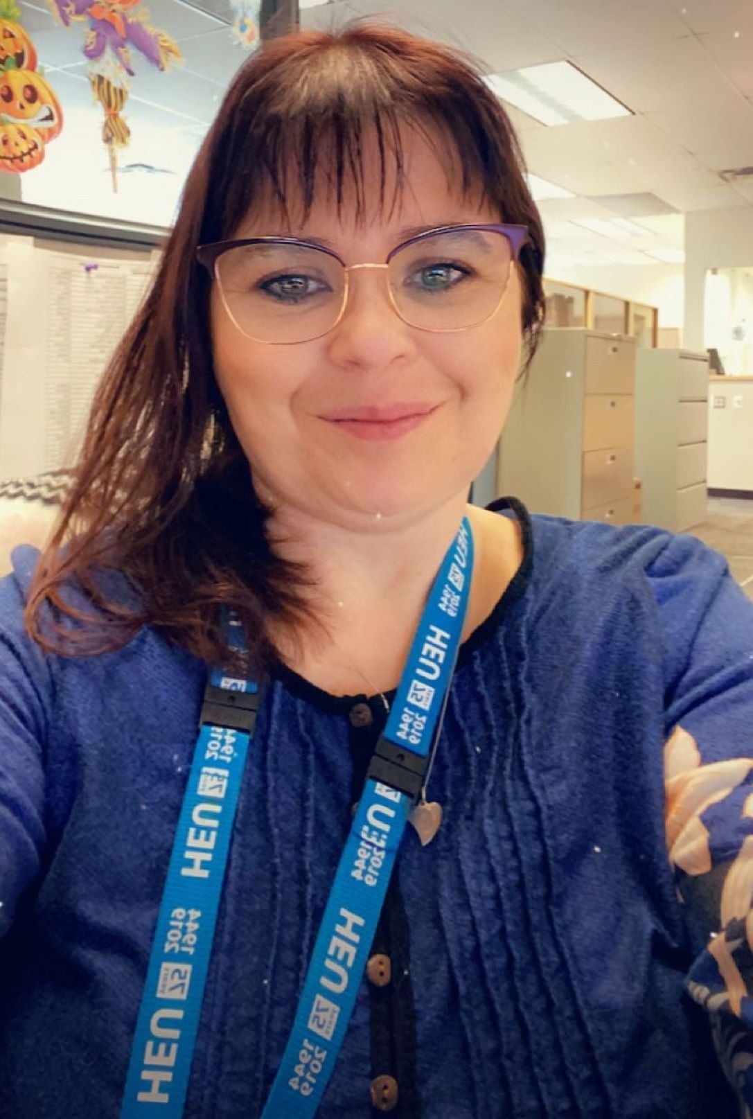 A woman wearing glasses is taking a picture of herself while sitting at her desk.  