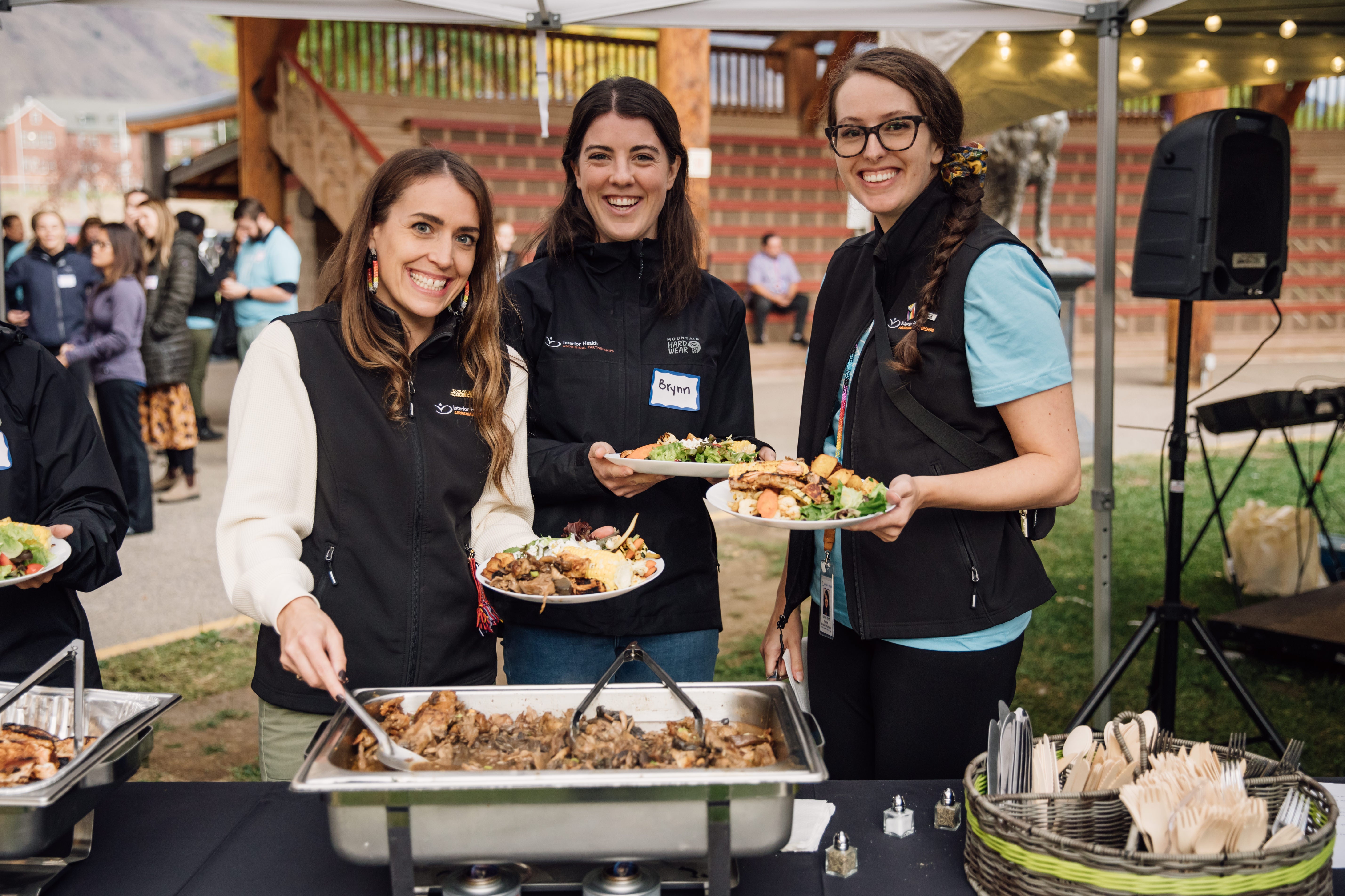 Three people holding plates of food in a buffet line.