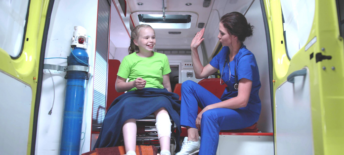 A nurse sits with a young patient in an ambulance and offers a high five to the patient.