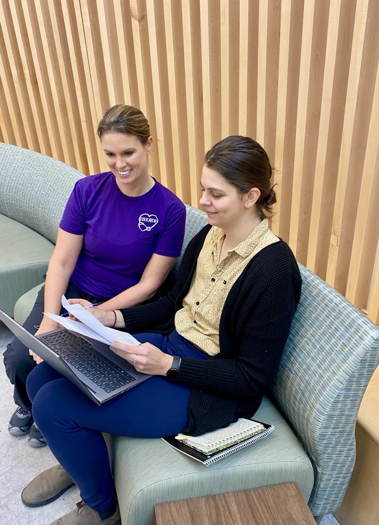 Two young people wearing casual clothes sit on a couch looking at a laptop and paperwork.