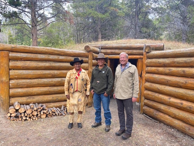 Three people pose in front of a wooden structure.