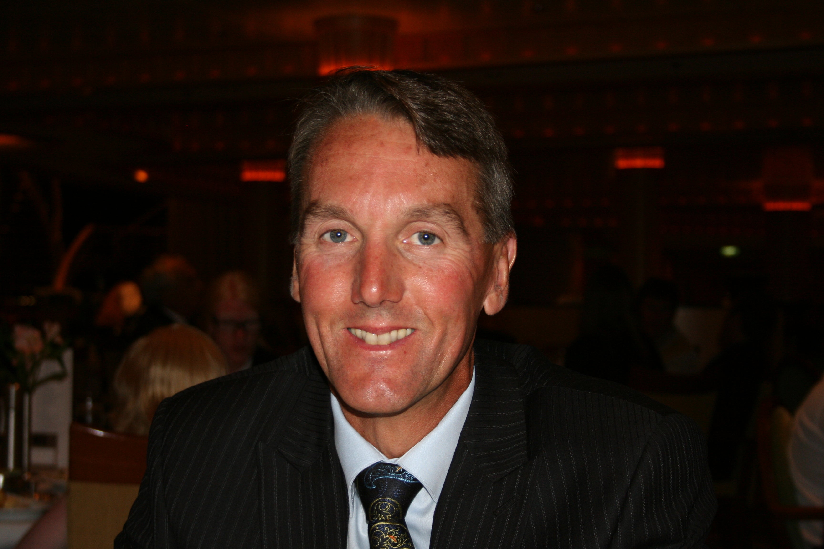 A person wearing a dark suit and patterned tie poses for a portrait at a formal event.