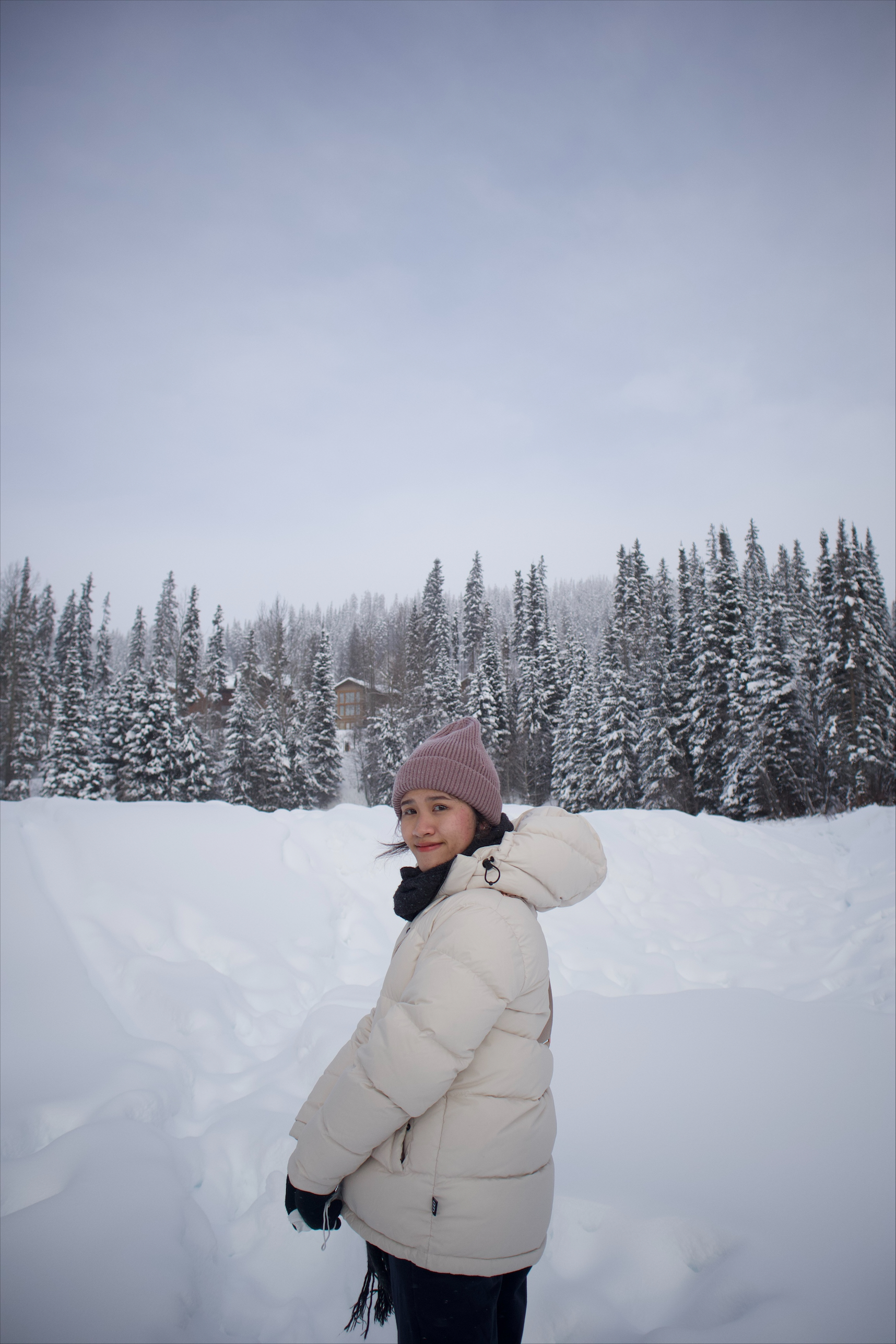 An individual is wearing a snow jacket and a pink toque surrounded by lots of snow and trees.  