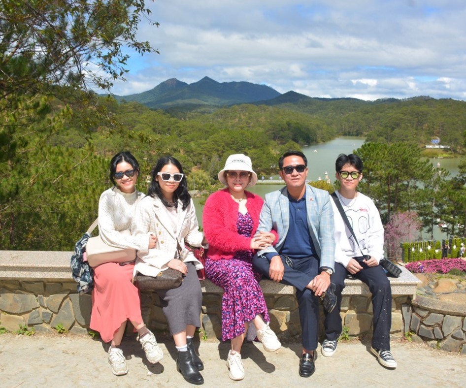  Five individuals are sitting on a ledge while mountains and forests cover the background of the photo. 