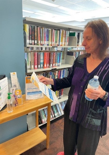 A person holding a bottle of water grabs a poster from a stand in front of a library bookshelf.