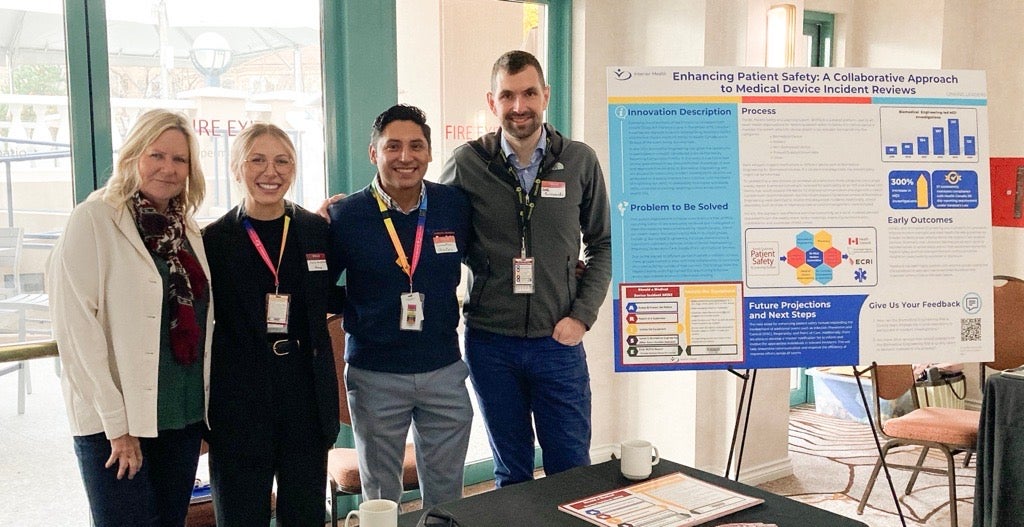 Four staff stand beside a patient safety poster at an indoor display table