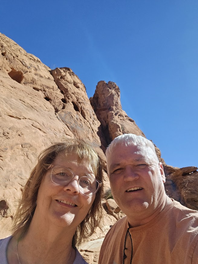 Two people pose in front of a desert wall.