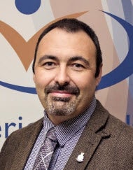 Man with dark hair and goatee smiles to camera. 