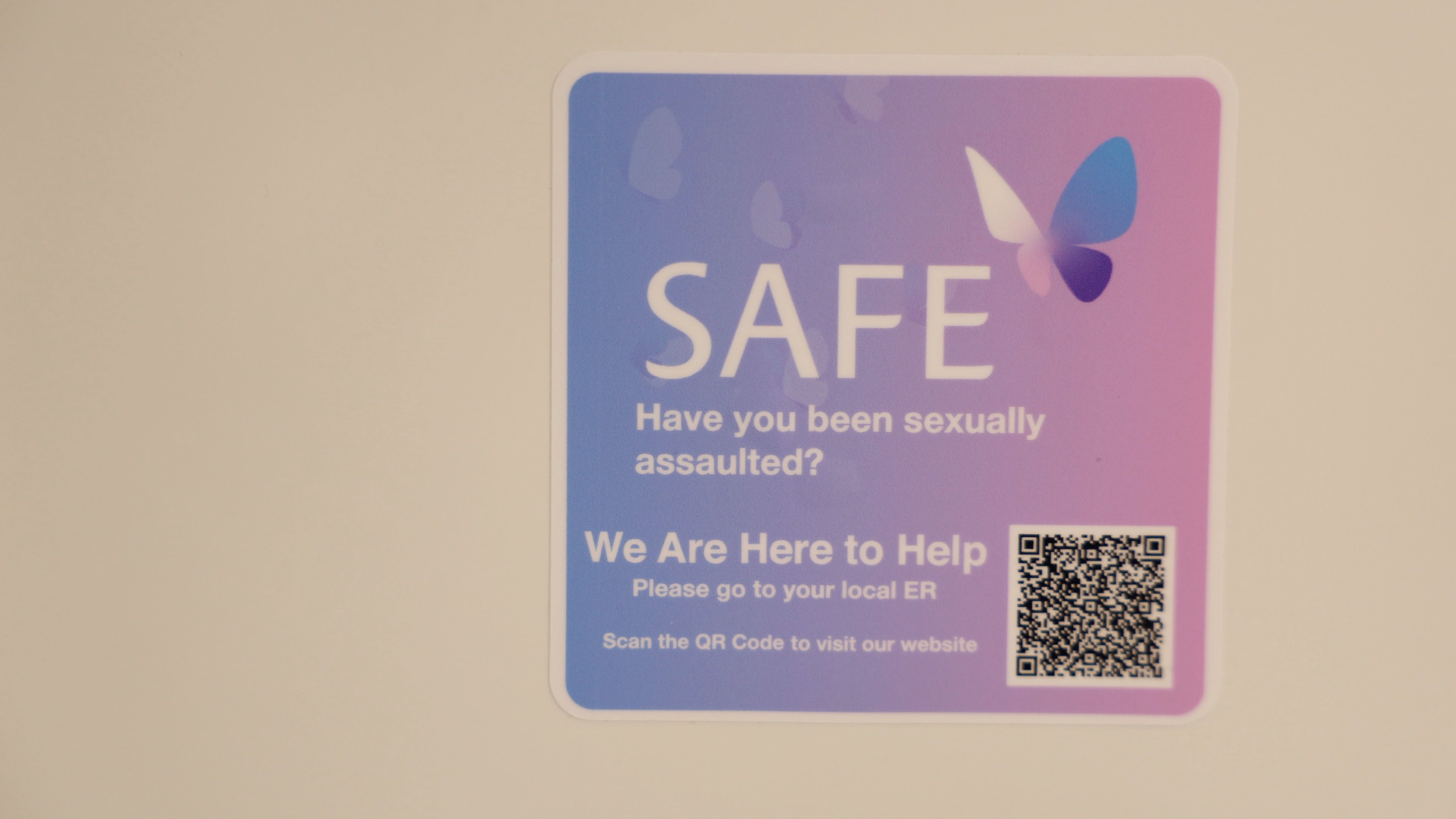 A blue and pink sticker with a butterfly and QR code. The text reads Have you been sexually assaulted? We are here to help. Please go to your local ER.