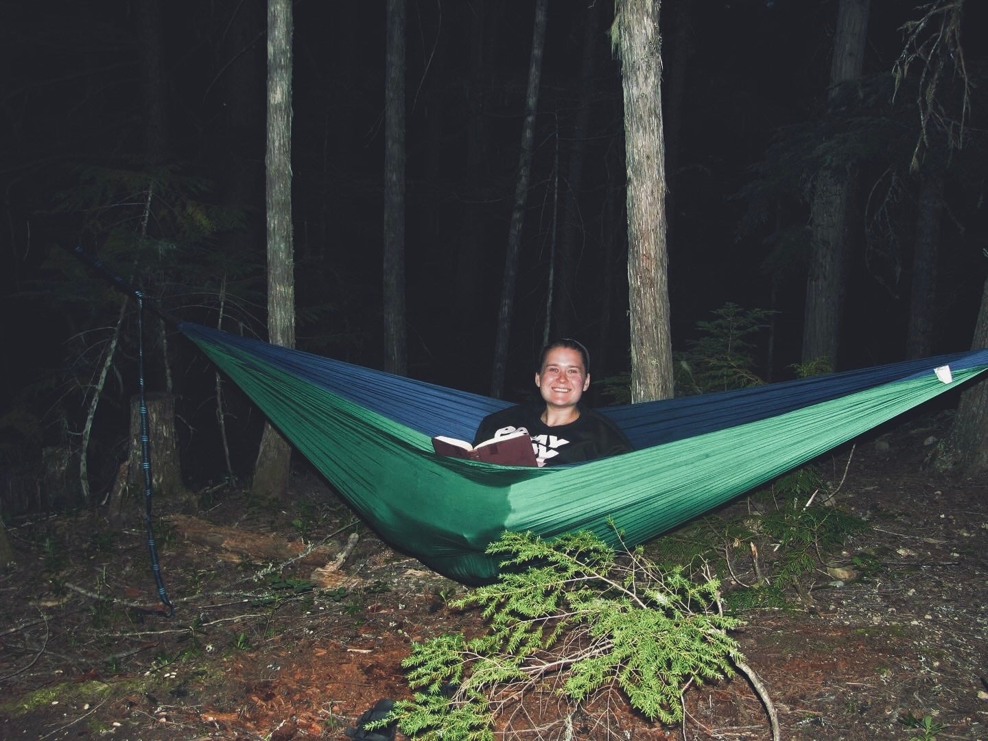 Person sits in a hammock and smiles while reading a book. 