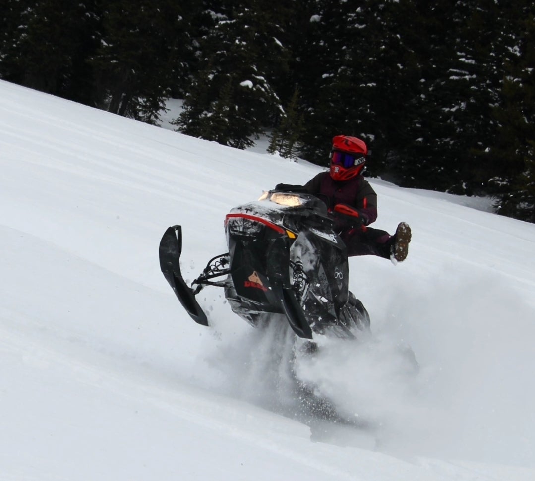 A person riding a snowmobile at high speed on a snowy terrain, performing a wheelie.