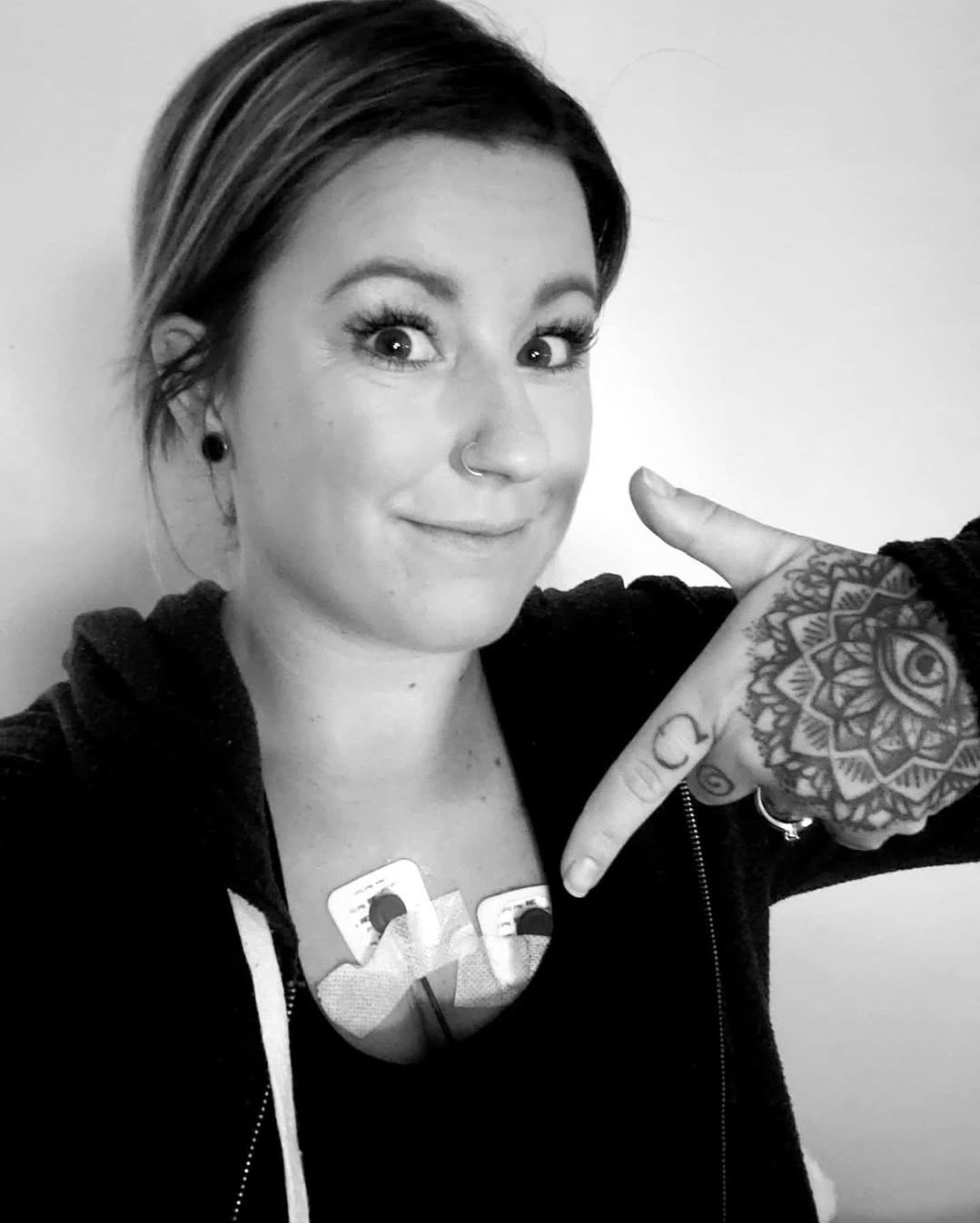 Person showing a tattoo of a geometric design on their hand, wearing a hoodie with the visible word "Love" and smiling at the camera.