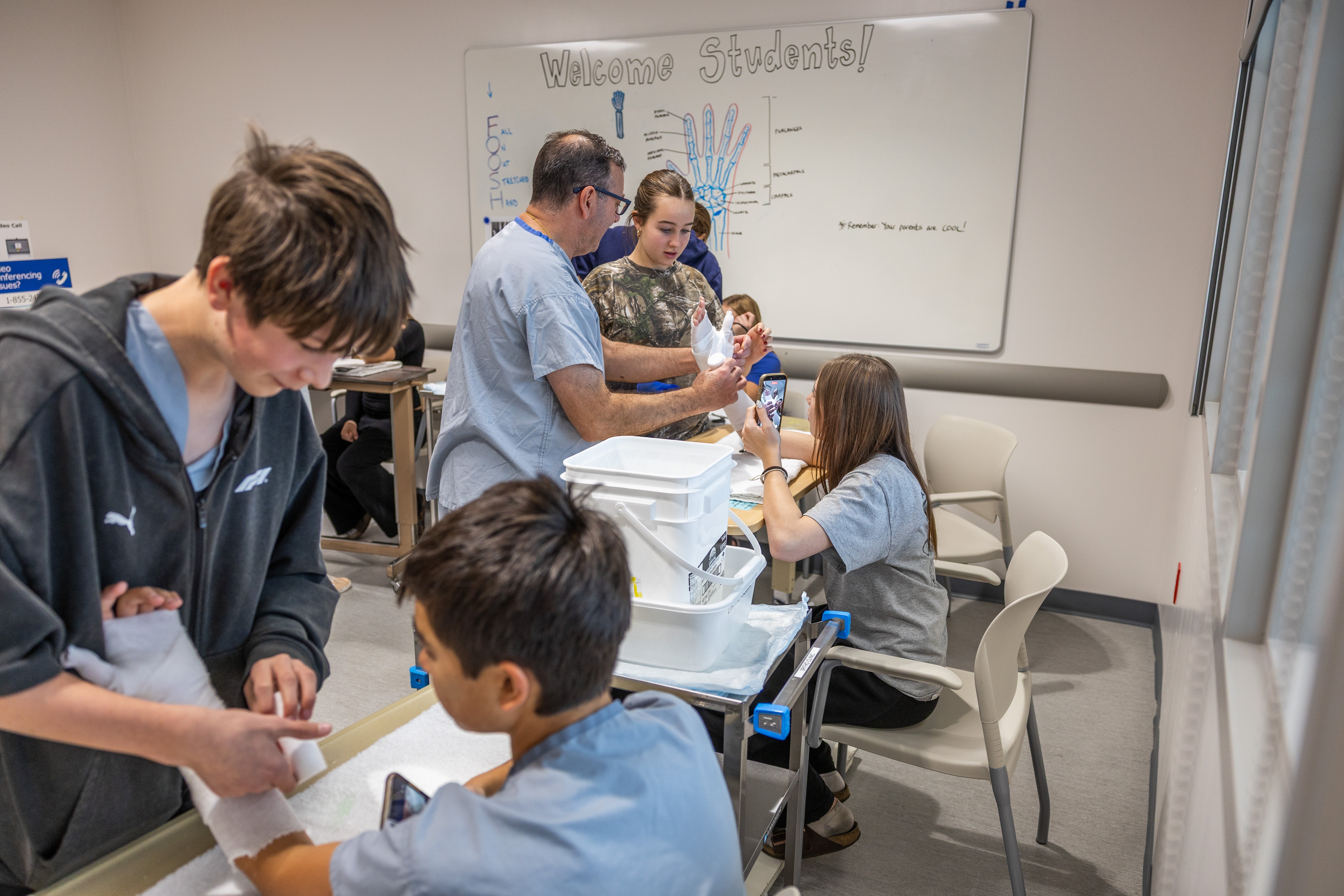 Young people and an adult in medical clothes practise putting casts on arms.