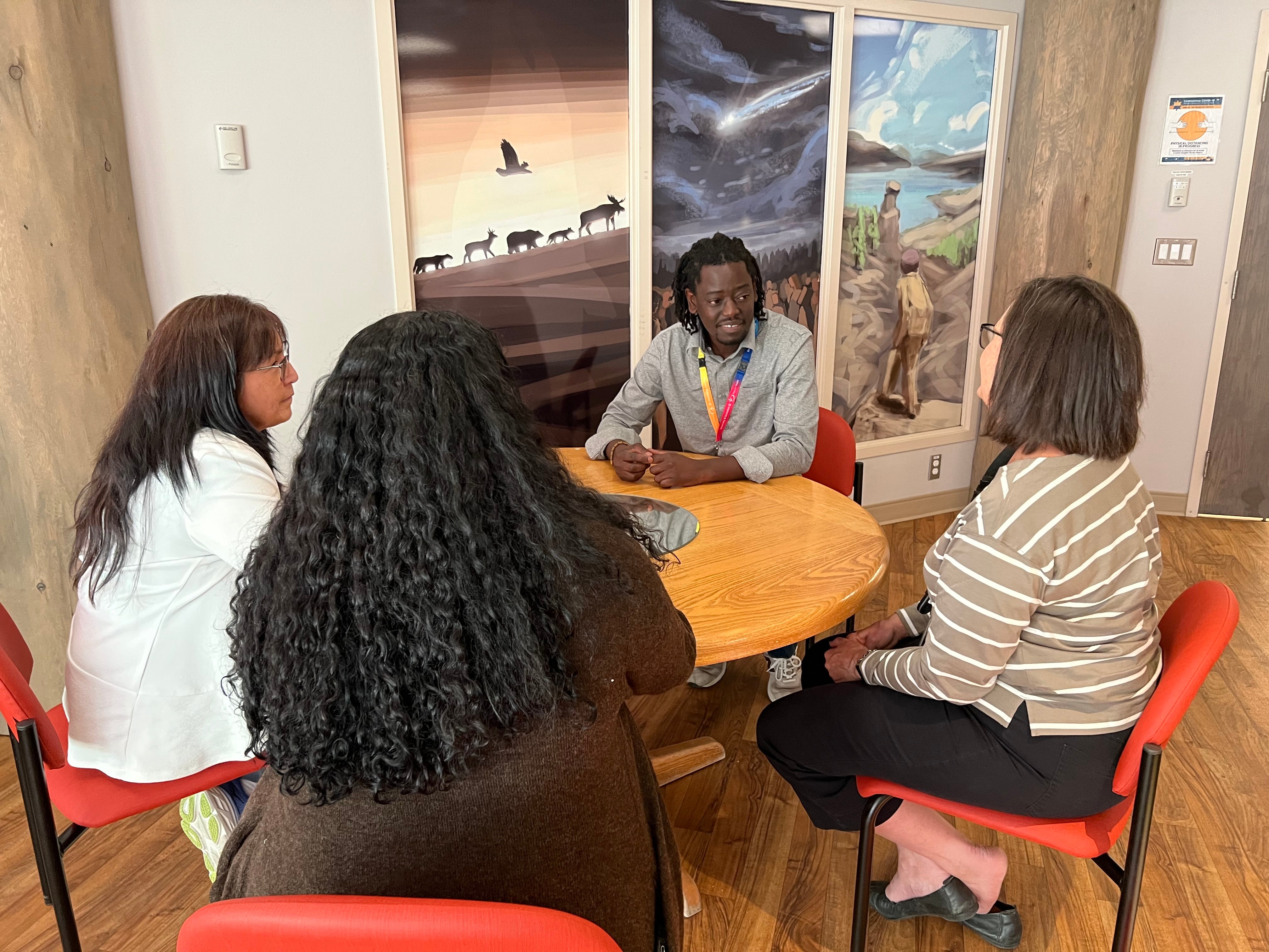 four people are sitting around a round table engaging in a discussion. 