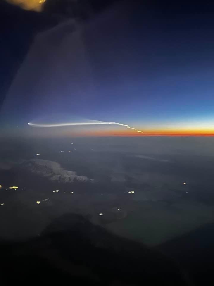 White streak trailing from a rocket launch during a sunset, as seen from a passenger airplane.