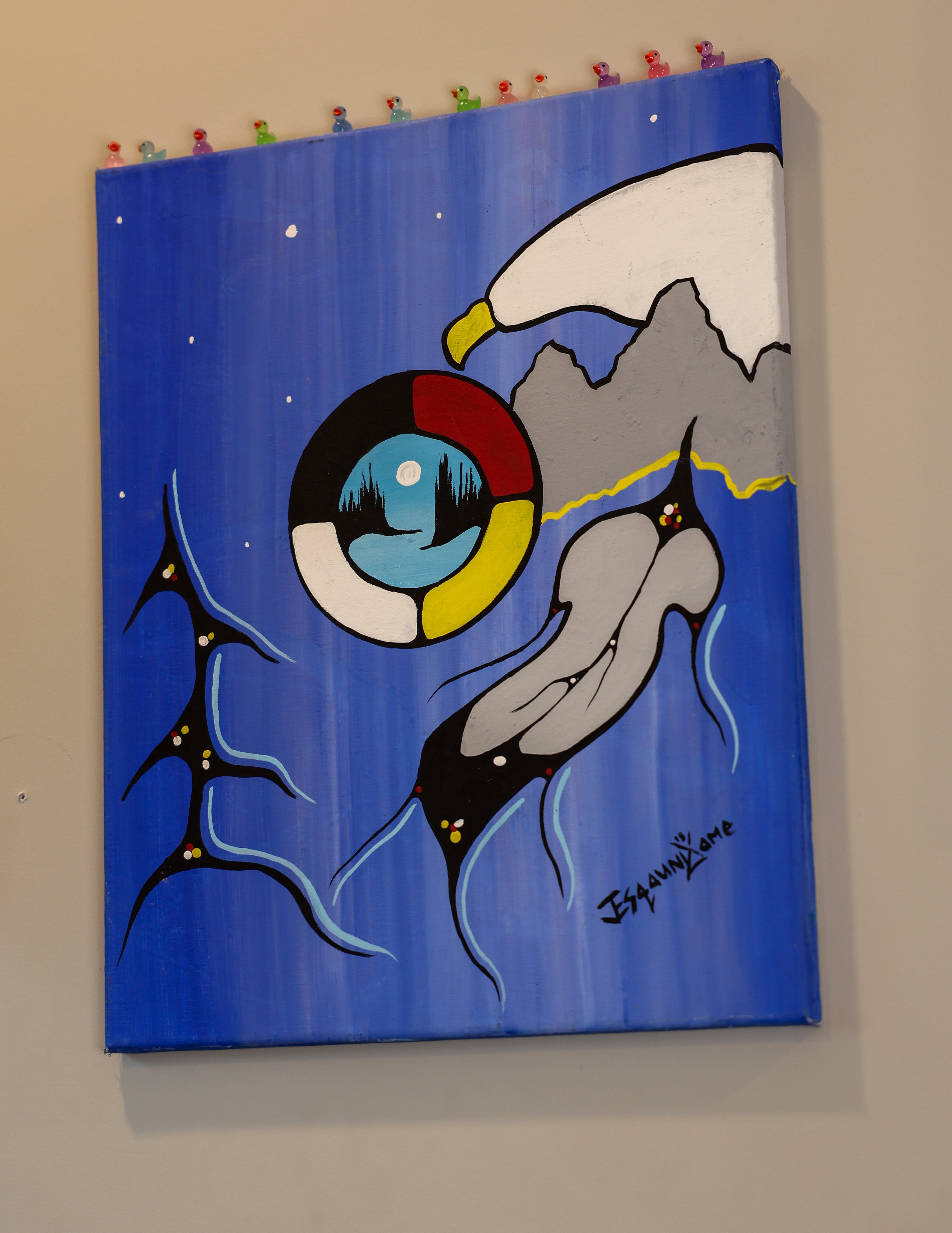 A painting hanging on a wall with blue background, a bird, a feather, and cultural symbolism. 