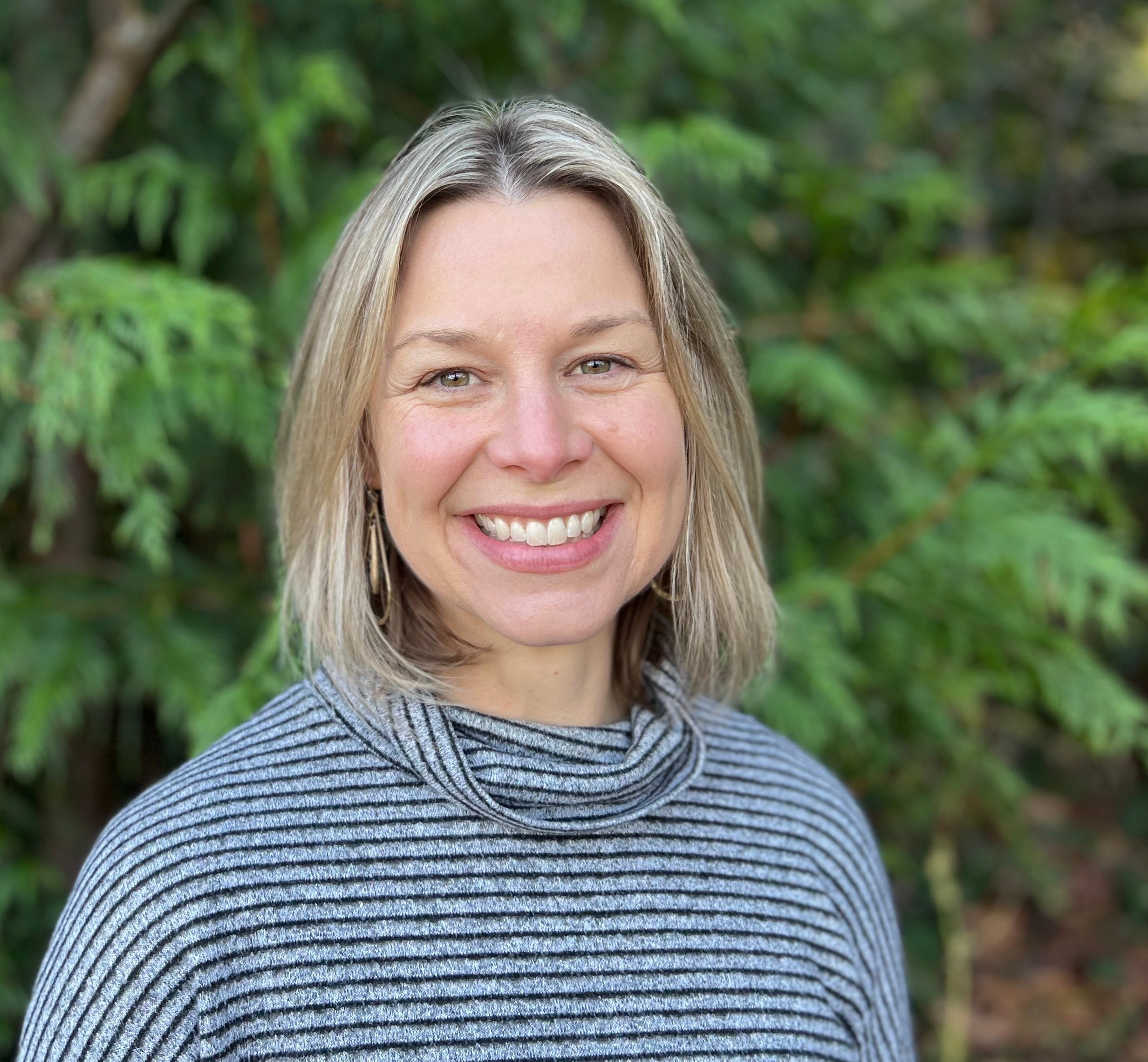 A person poses outside for a picture with a tree in the background.