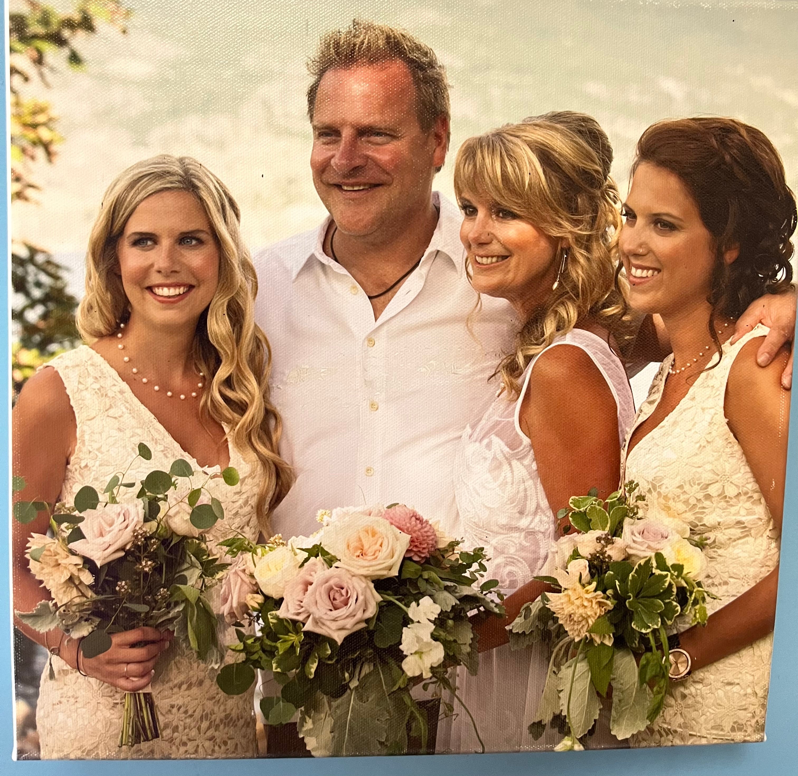 A married couple in white clothes stand next to two people in cream dresses holding bouquets of roses