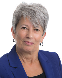 A profile shot of a woman with grey hair who is wearing earrings and a blue business suit.