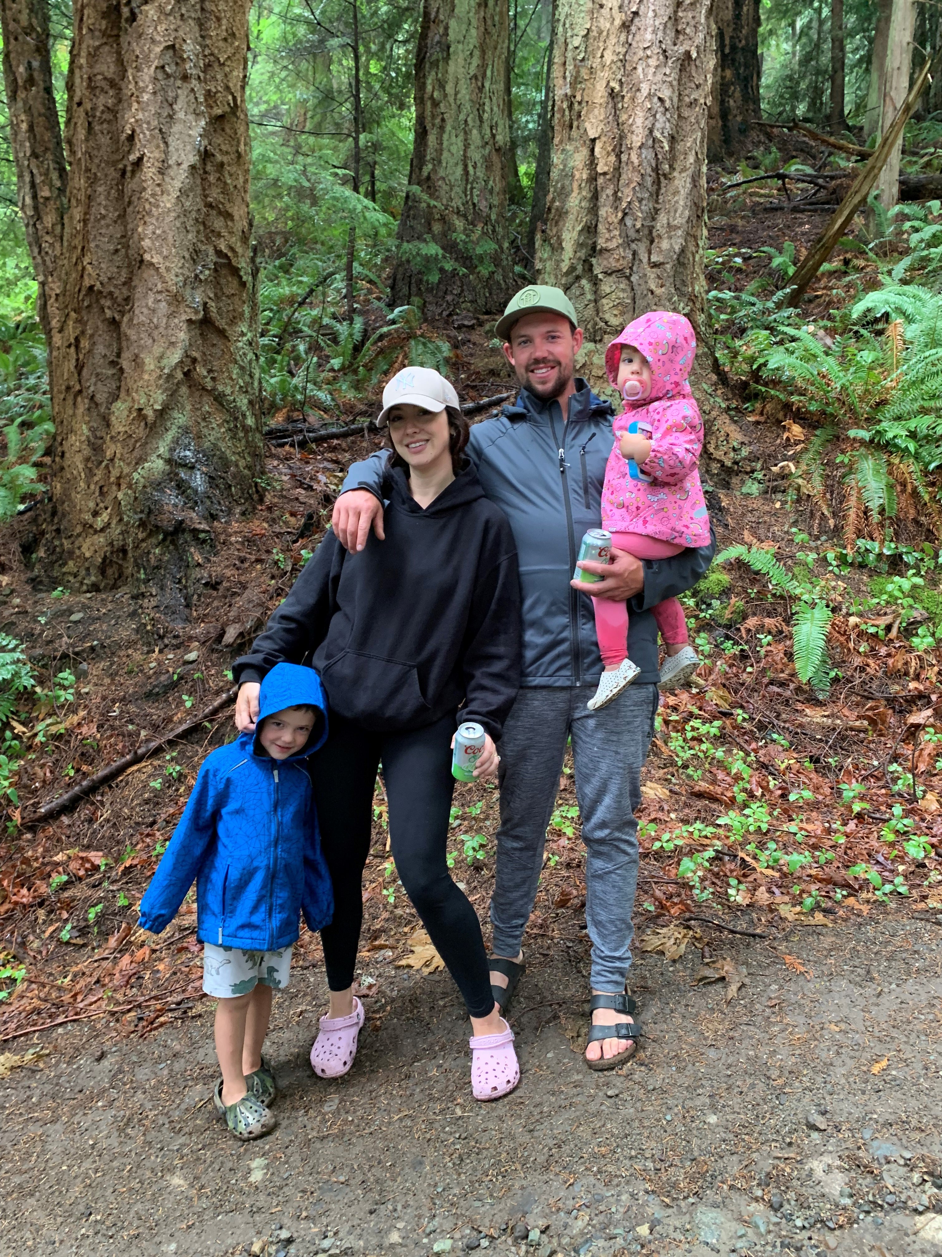 A woman and man in warm clothing and hats pose with two children in a forest