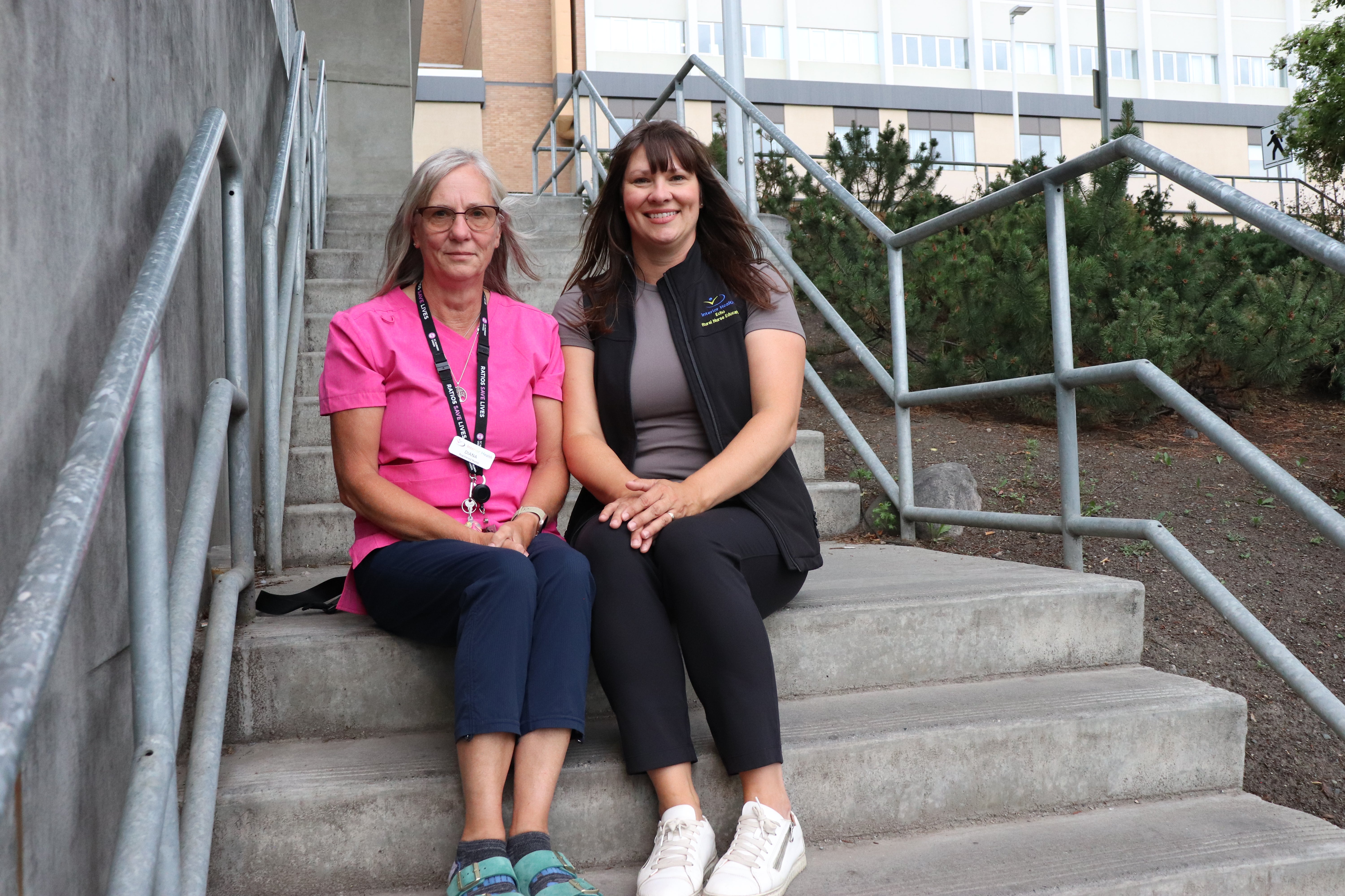 Two people sit side by side on concrete steps in front of a building.