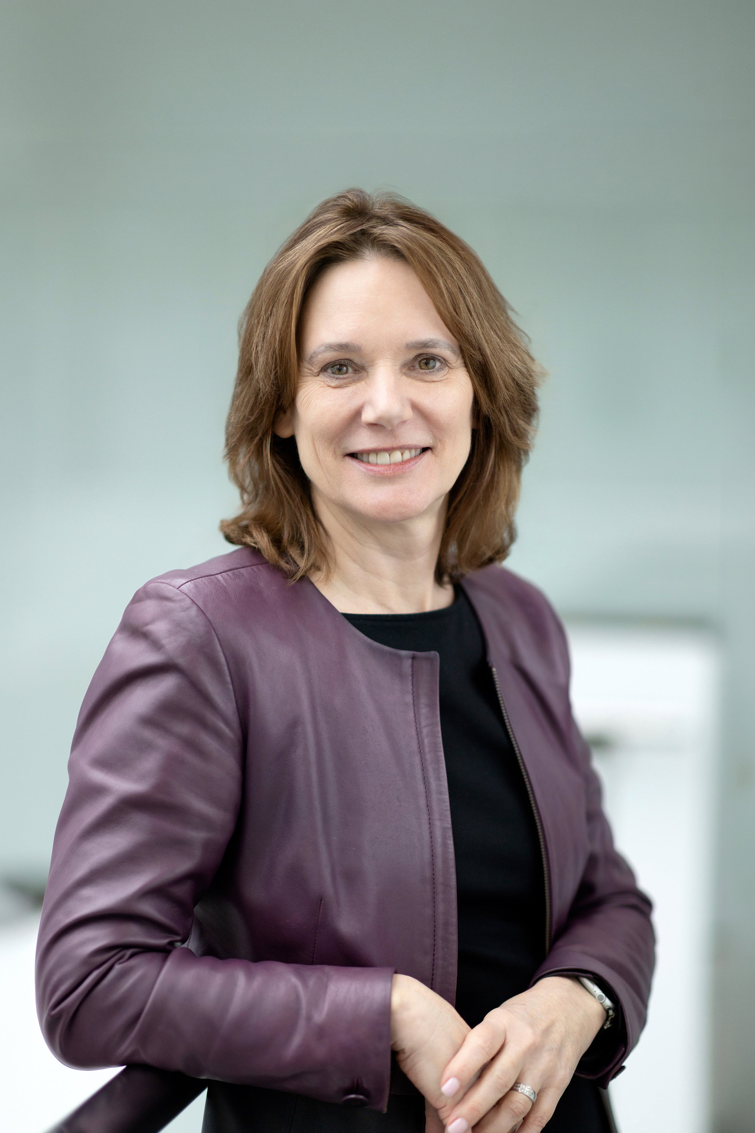 Profile shot of a smiling person with mid length brown hair wearing a black shirt and purple blazer.