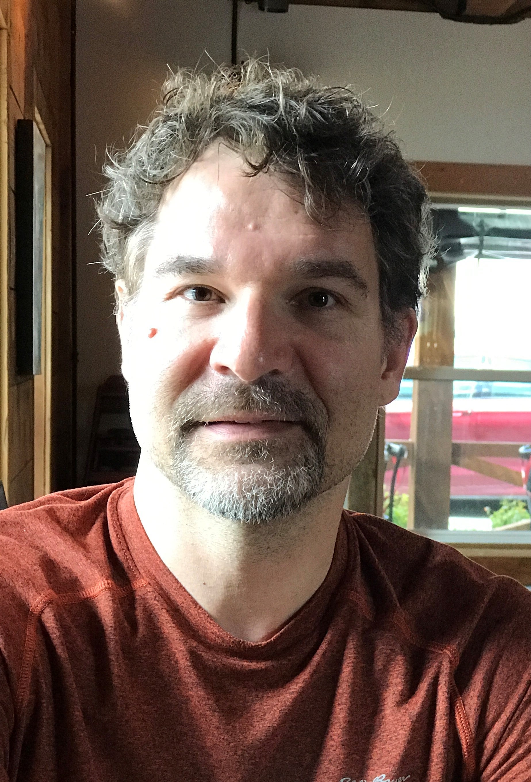 Man with short, dark hair, goatee, and red t-shirt looks to camera. 