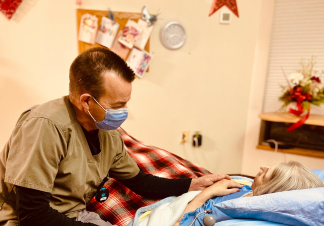 A man wearing a medical mask and scrubs comforts a patient who is laying down.