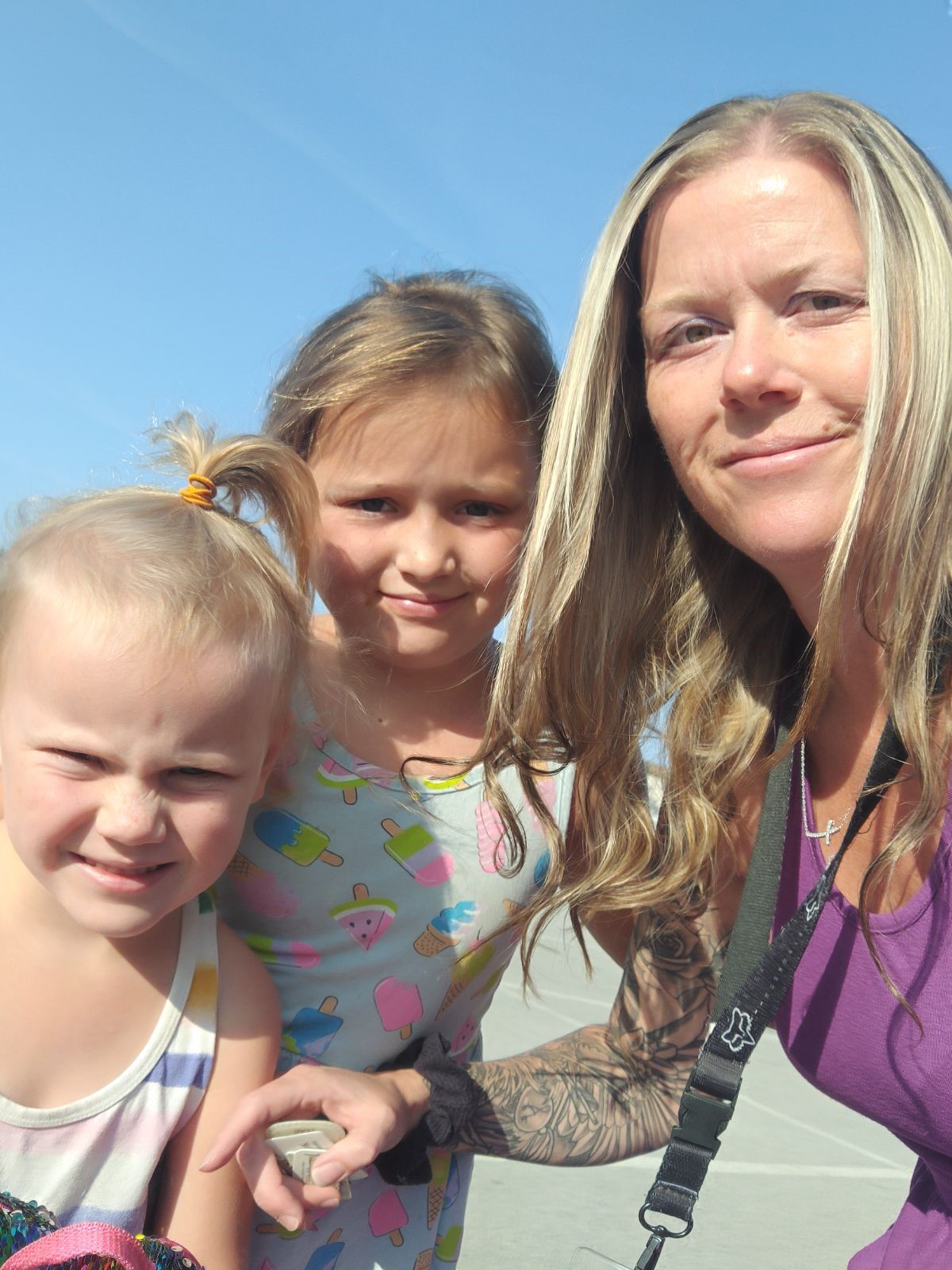 A woman with blonde hair and wearing a purple top takes a photo with a blonde child, and blonde  toddler