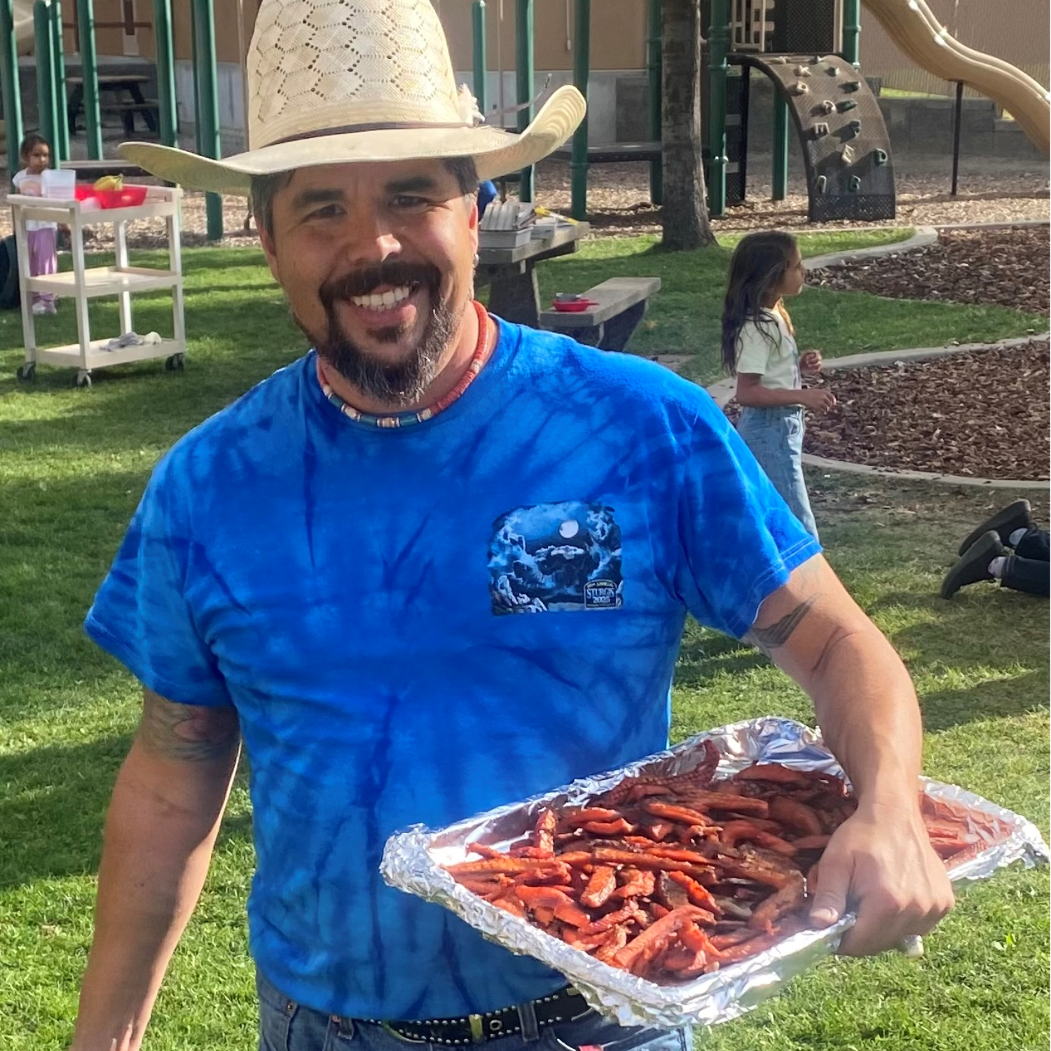 a person wearing a hat and blur shirt holds a tray of vegetables
