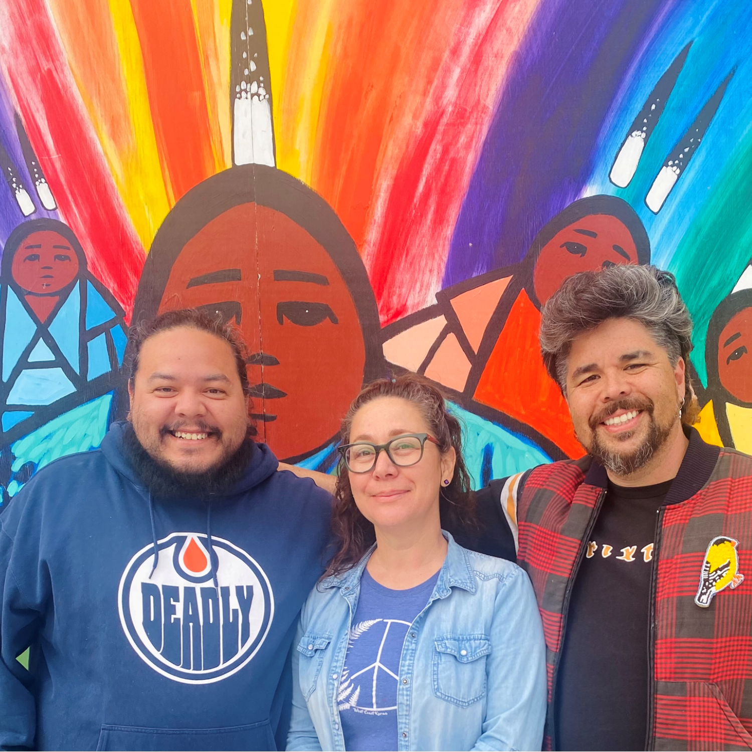 three people stand in front of a colourful mural and smile